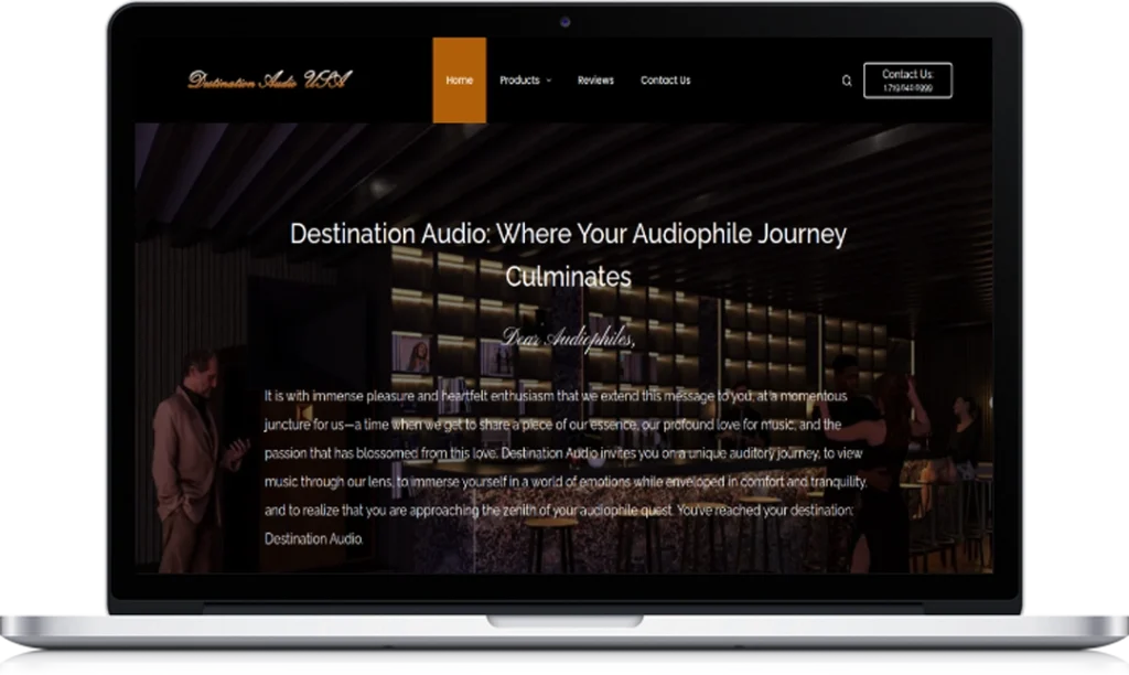A laptop displays the homepage of Destination Audio, featuring a dark-toned interior photo, navigation menu, company logo, and highlighted text describing a premium audiophile experience.